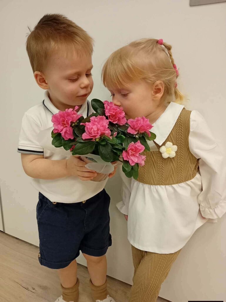 Strona główna 3 Chłopiec i dziewczynka wąchają różowe kwiaty w doniczce
