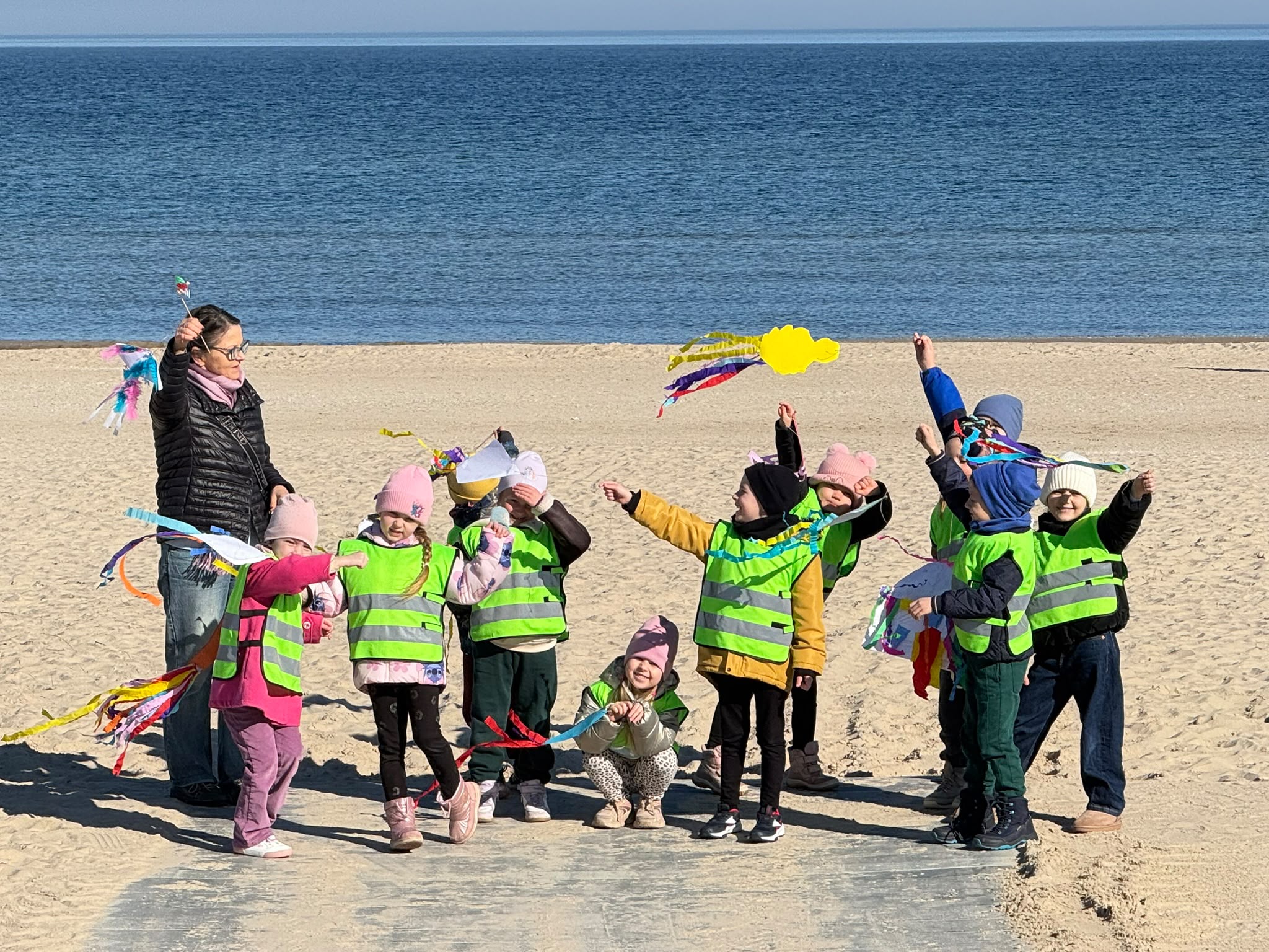 Strona główna 1 Grupa przedszkolaków w kamizelkach odblaskowych bawi się na plaży nad morzem