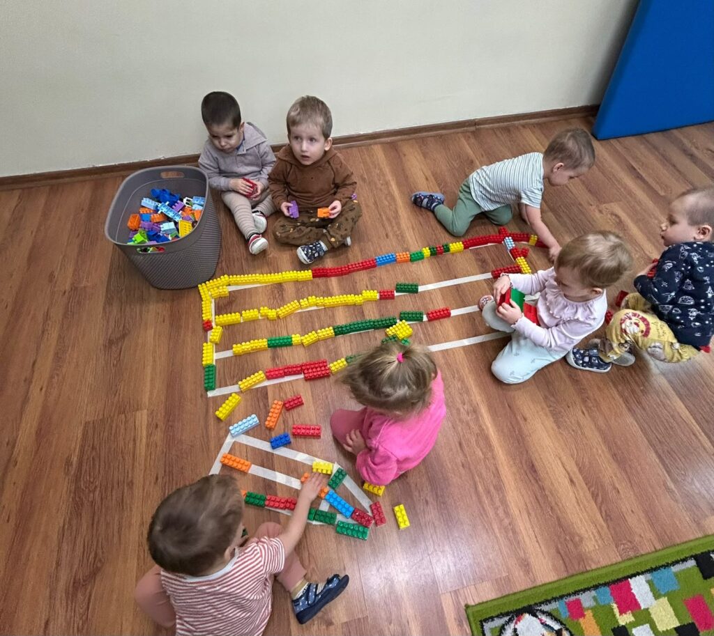 Strona główna 6 Maluchy układają długi rząd kolorowych klocków na podłodze sali